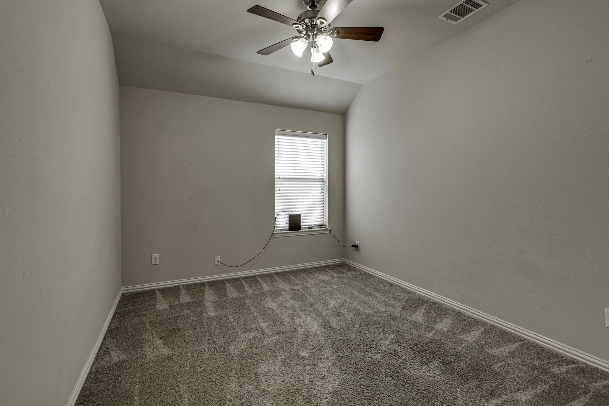 Vaulted ceiling with a ceiling fan light fixture, single window with blinds, and neutral tone carpeting