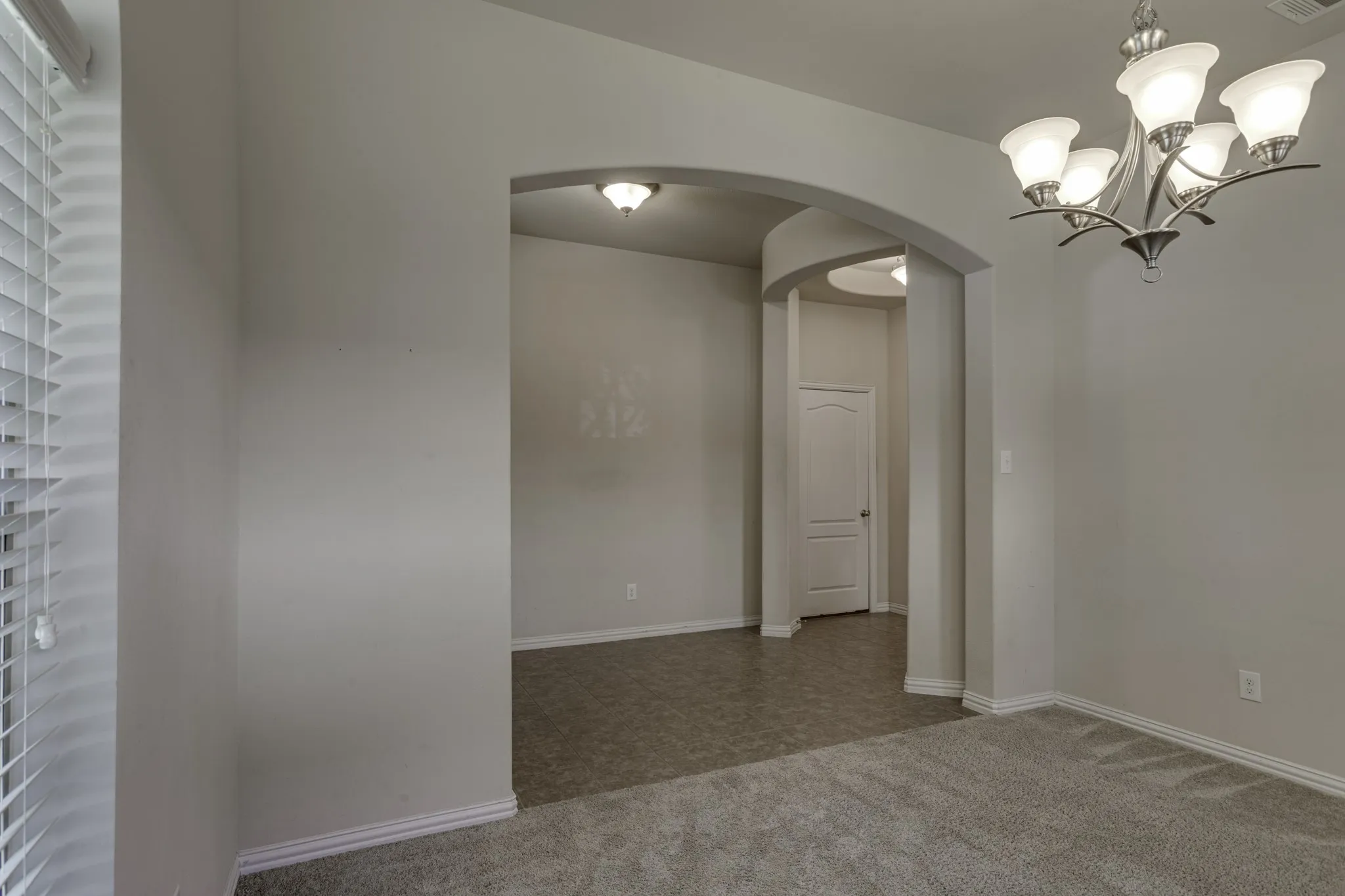 Living or ding as you enter, that features and arched doorways frame interior spaces, complemented by a multi-bulb chandelier and window blinds.