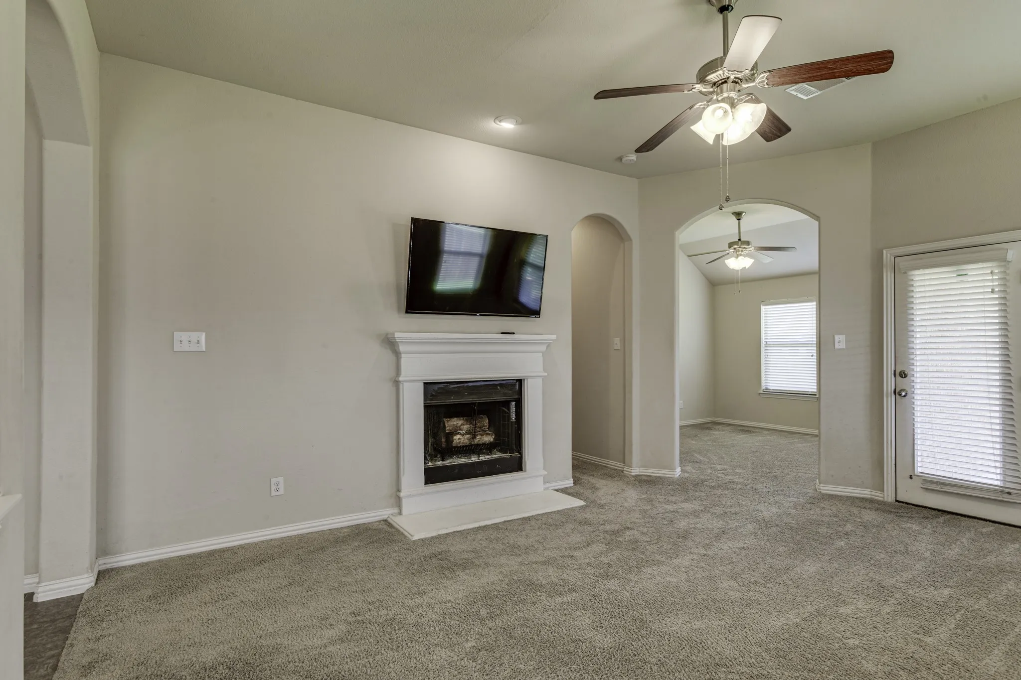 Living area featuring a fireplace with a white mantel, ceiling fans, and an arched doorway.