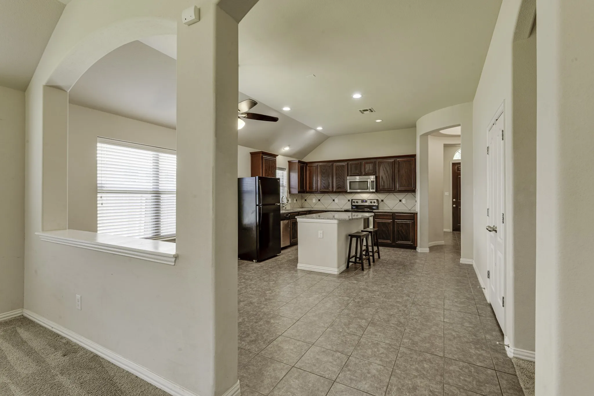 Open-concept kitchen and dining area featuring dark wood cabinetry, stainless steel appliances, a large center island with seating, tile flooring throughout, and abundant natural light from multiple windows