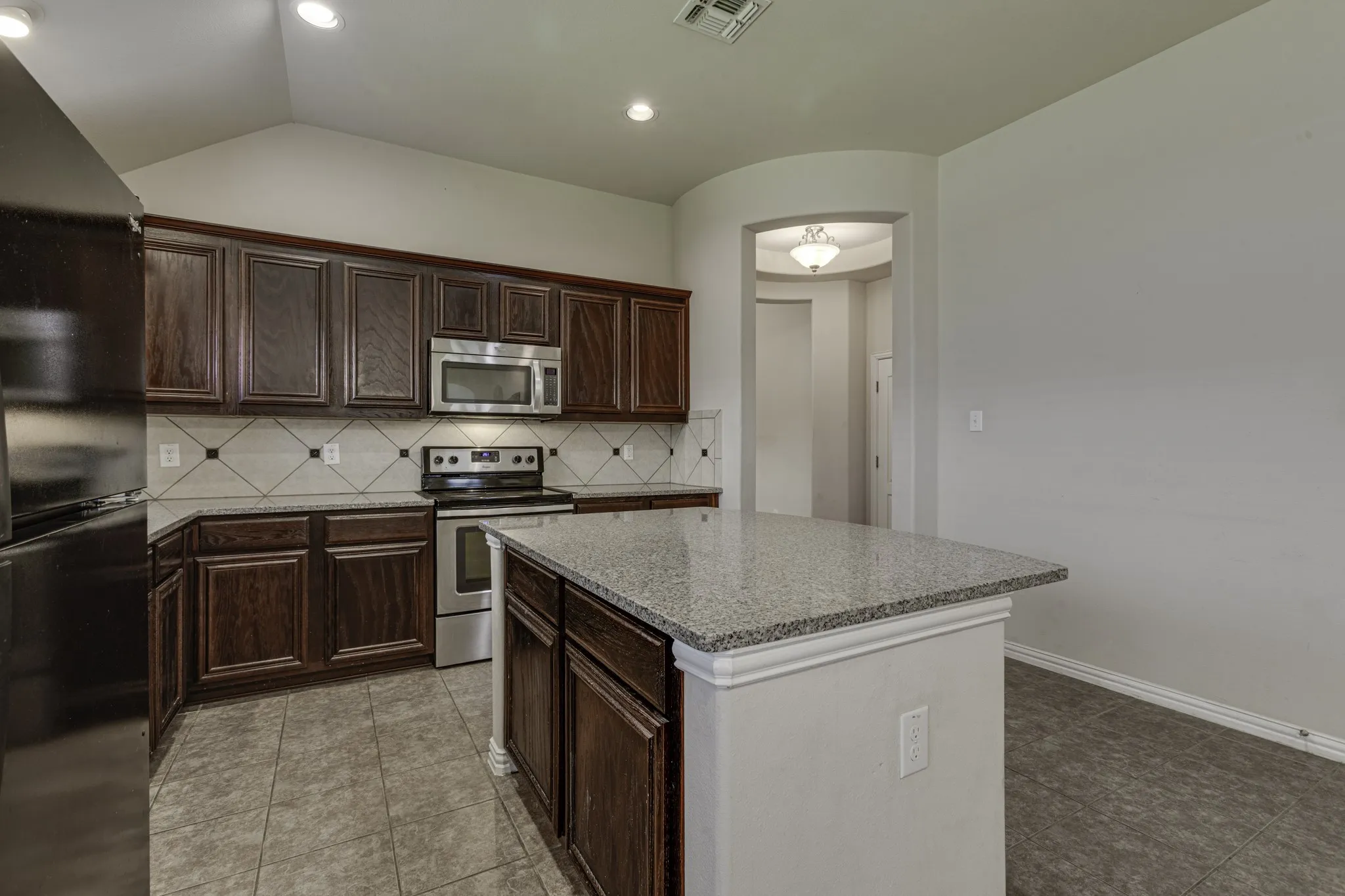 Kitchen with dark wood cabinetry, stainless steel appliances, granite countertops, and tile flooring