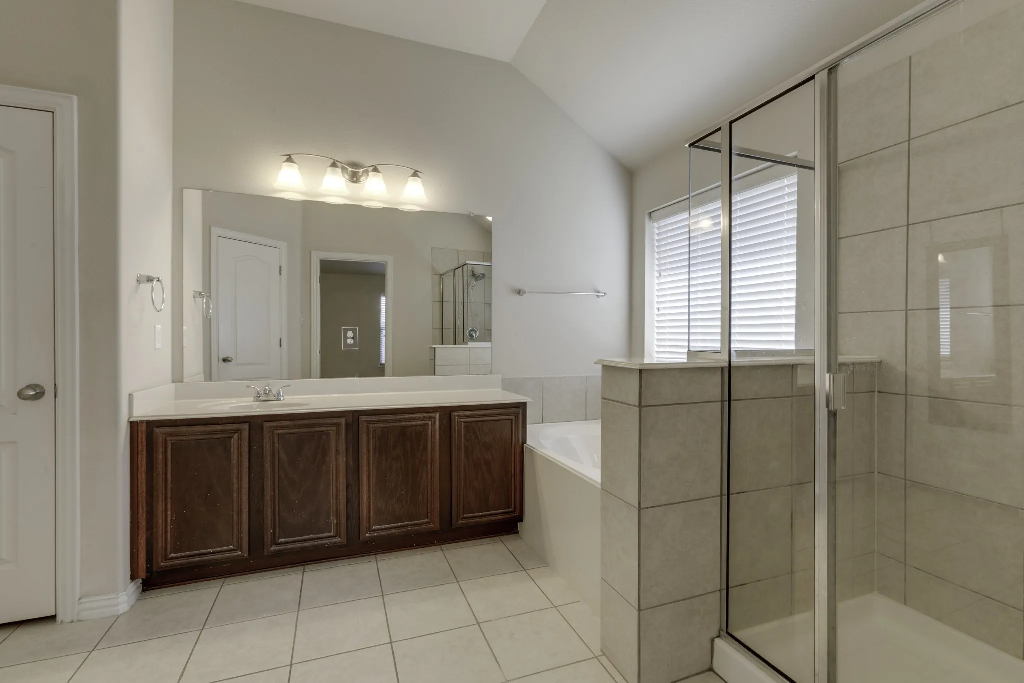 Spacious master bathroom featuring a large vanity with ample storage, an expansive mirror, a built-in bathtub, a separate glass-enclosed shower, and tiled flooring.