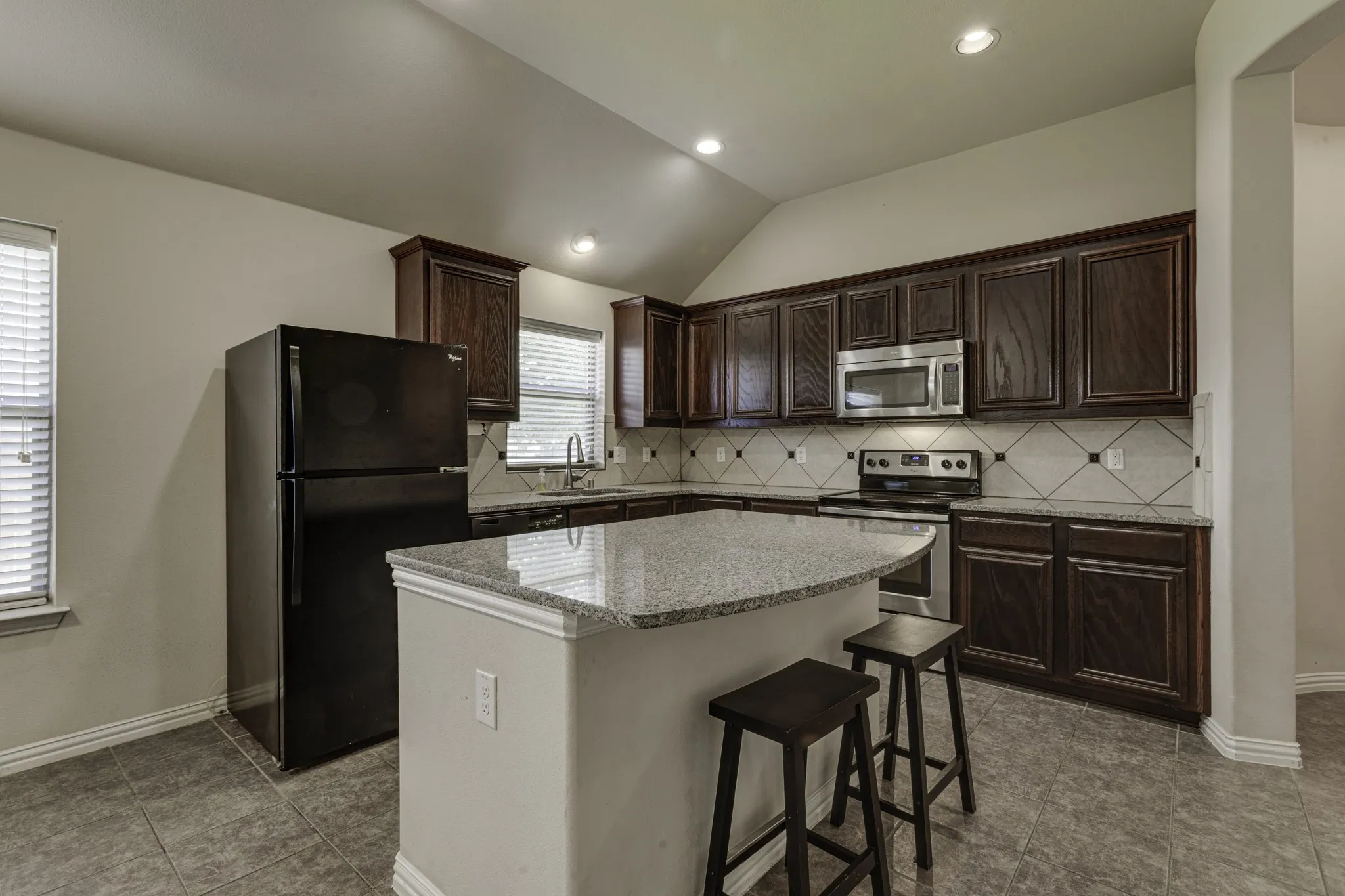 Modern kitchen featuring dark wood cabinetry, stainless steel appliances, and a large quartz-topped island with seating for two