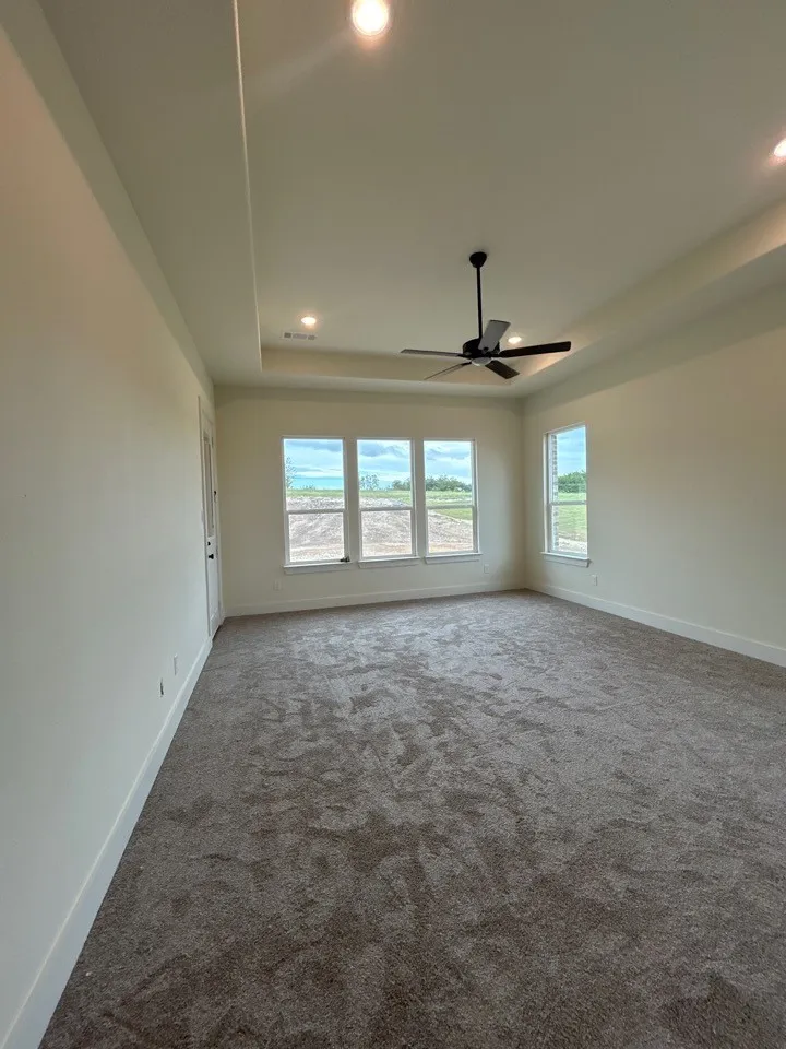 Tray ceiling with recessed lighting, ceiling fan, expansive windows, and plush carpet