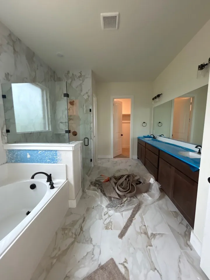 Dual vanity with dark wood-finish cabinetry, floor-to-ceiling tiled shower enclosure with a clear glass door, built-in bathtub, and large format tile flooring