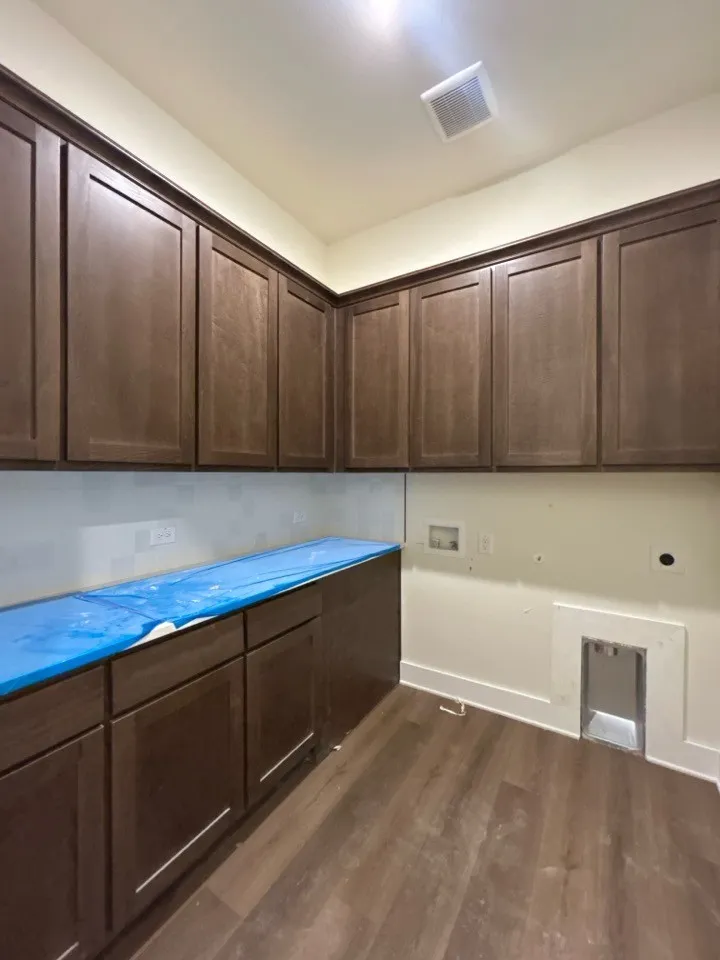 Extensive cabinetry with dark wood-finish, light-toned backsplash, wood-finish flooring, and a built-in dryer vent