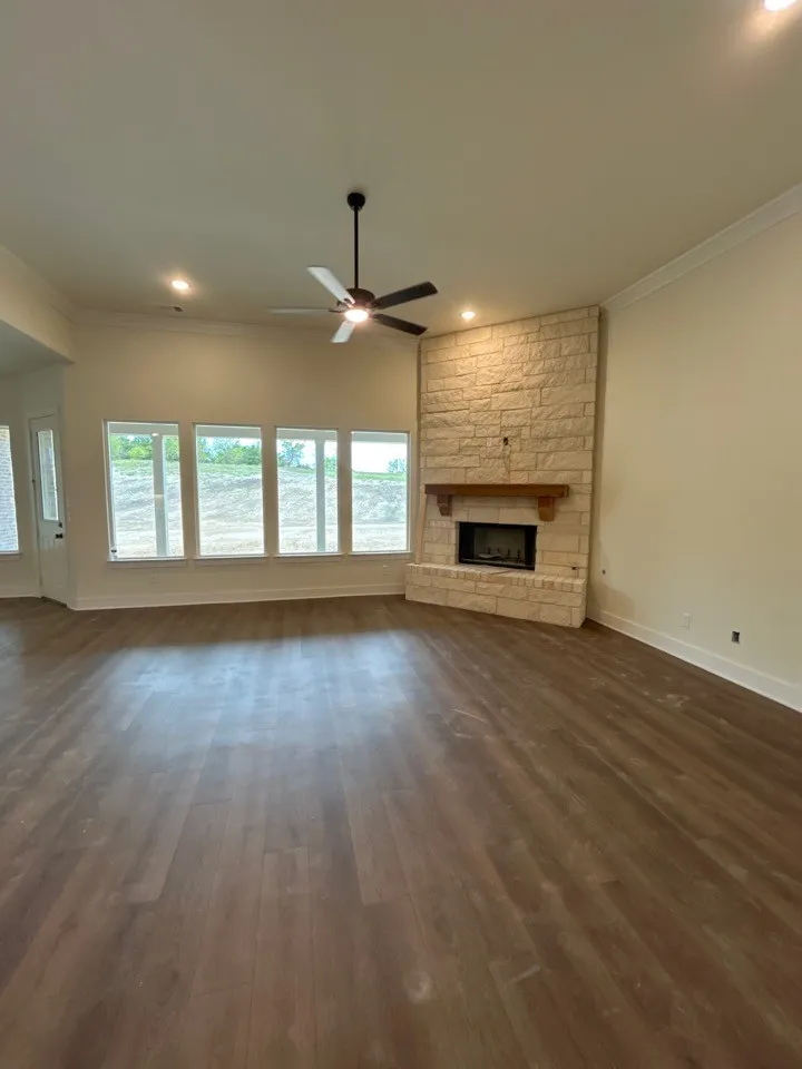 Corner stone-clad fireplace with wood mantle, wood-finish flooring, recessed lighting, ceiling fan, and multiple windows
