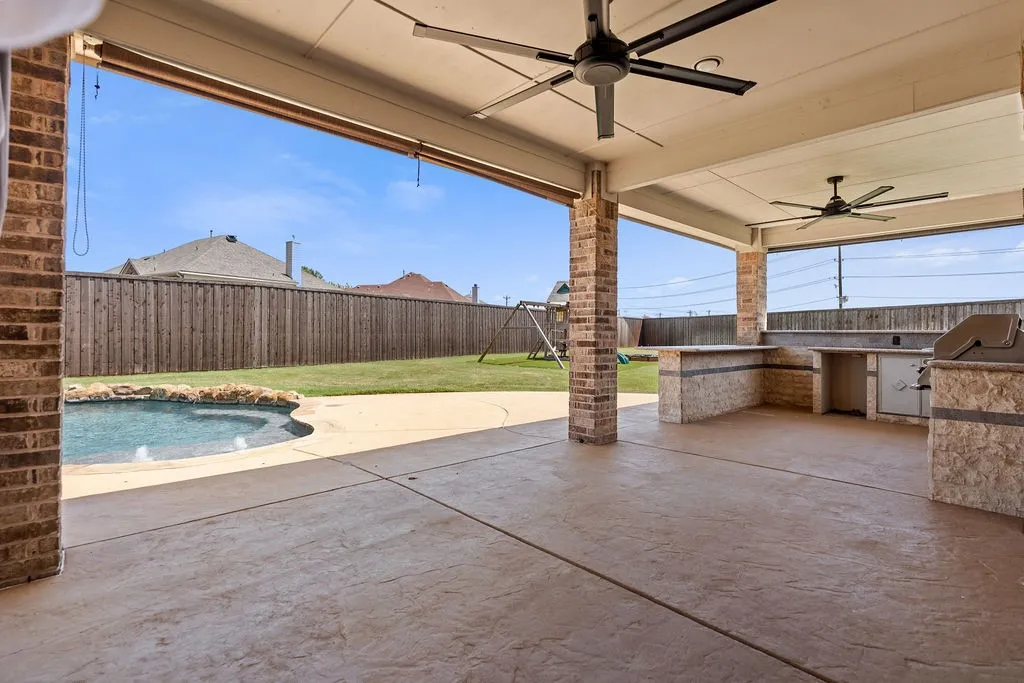 Covered patio featuring an outdoor kitchen, two ceiling fans, brick columns, and direct access to a swimming pool