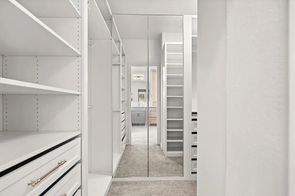 Custom closet system with white shelving, integrated drawers with brass hardware, and full-length mirrored doors