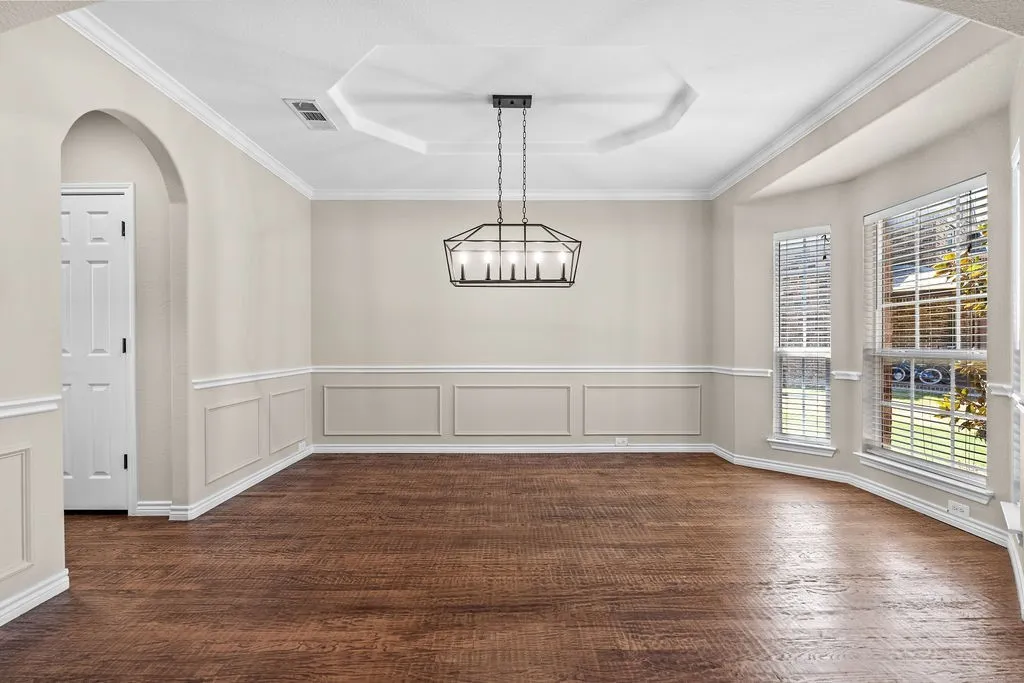 Wood-finish flooring, accent wall paneling, vaulted ceiling with a geometric chandelier, and multiple windows with blinds