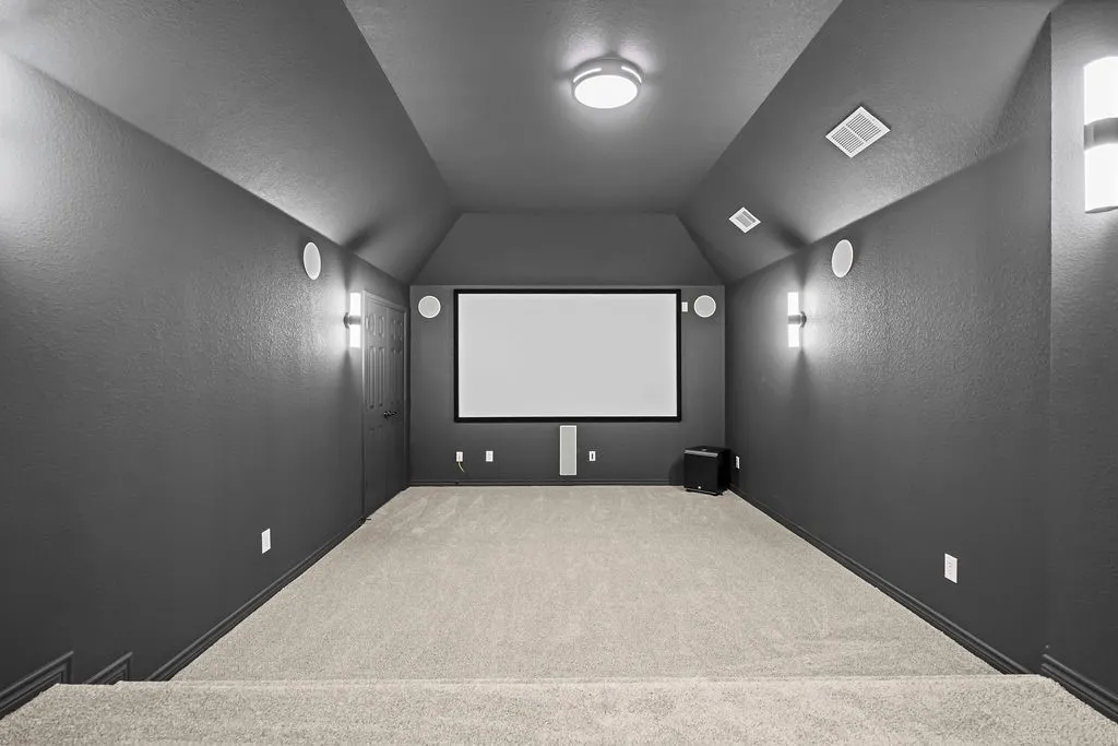 Dedicated media room featuring a large projector screen, built-in speakers, wall-mounted sconces, and recessed ceiling lighting