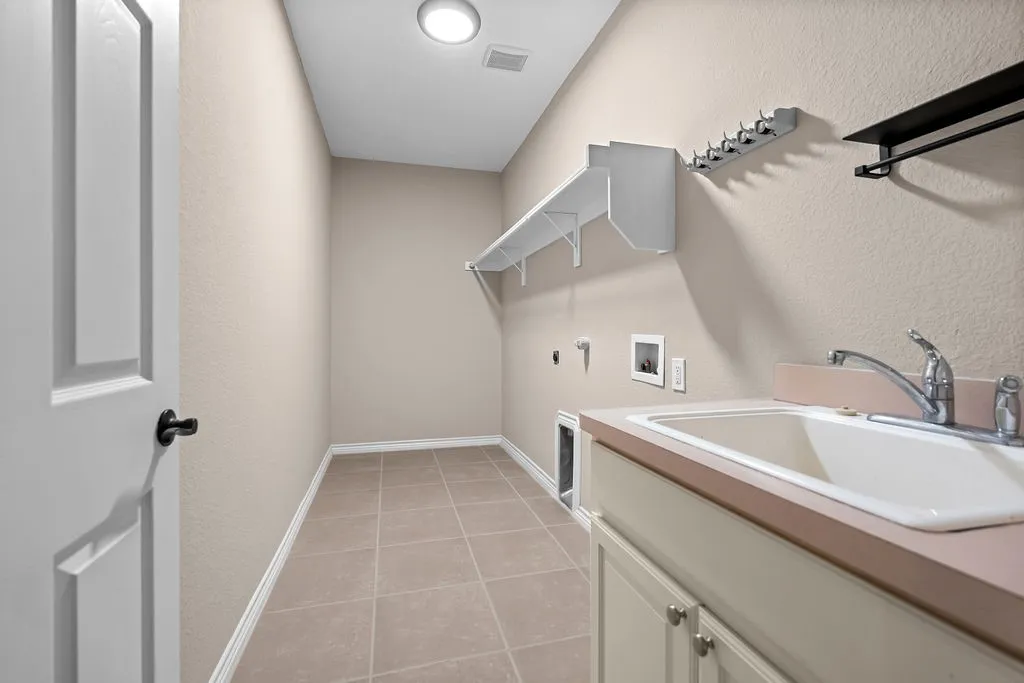 Utility room featuring a built-in sink, cabinet storage, wall-mounted shelving, and tile flooring