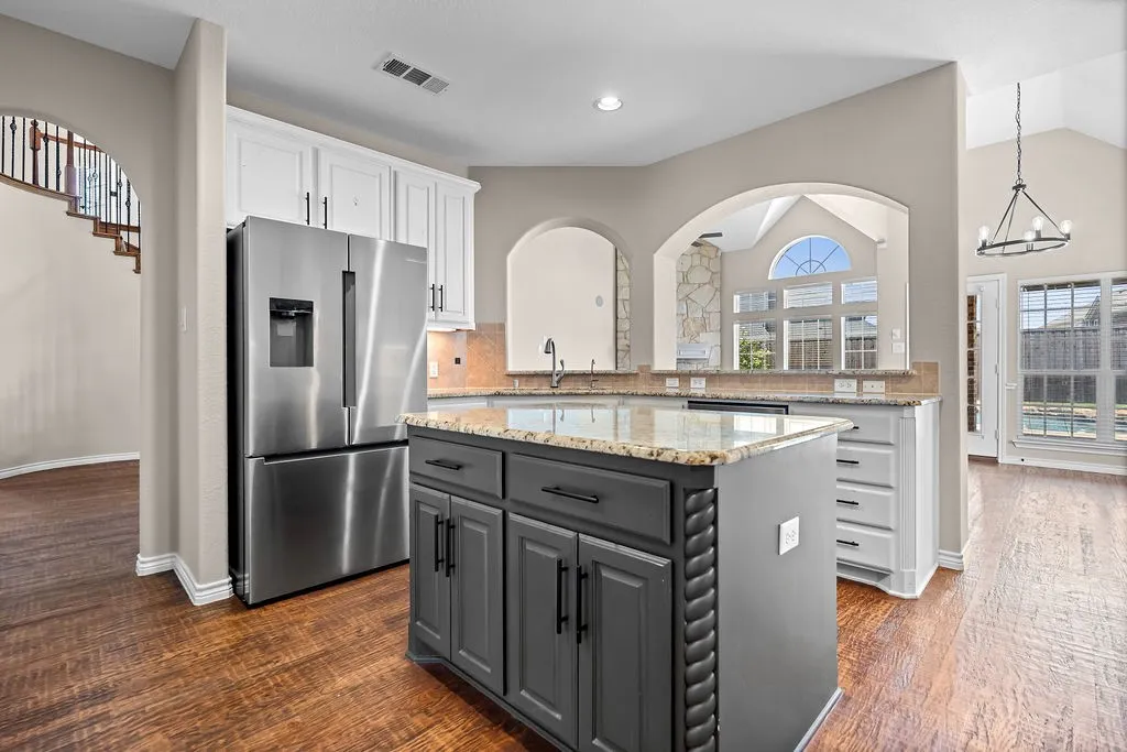 Kitchen island with a granite countertop and storage, stainless steel refrigerator, wood-finish flooring, white cabinetry, and arched architectural openings
