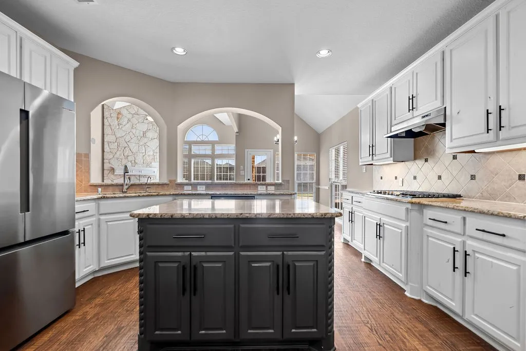 White cabinetry, wood-finish flooring, central island with dark finish, stone countertops, and stainless steel appliances