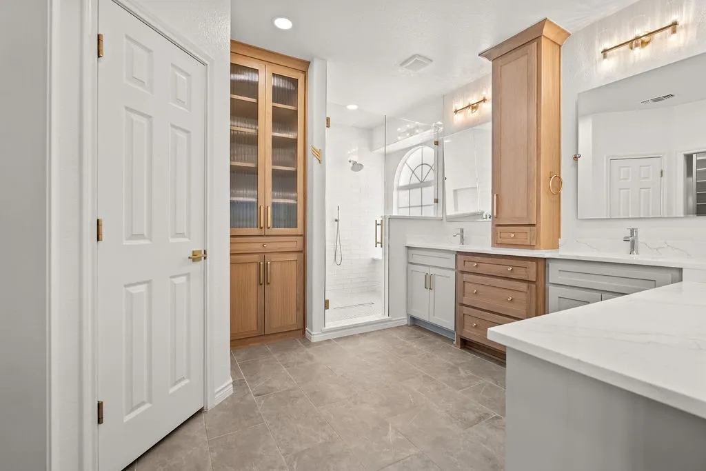 Dual vanity with integrated sinks, glass-enclosed shower with subway tile surround, built-in storage cabinetry, and tile flooring