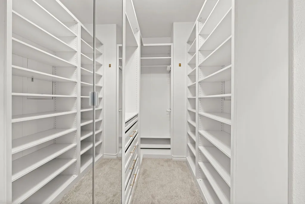 Custom built-in shelving, mirrored closet door, built-in dresser with brass hardware, clothes hanging rod, and neutral tone flooring