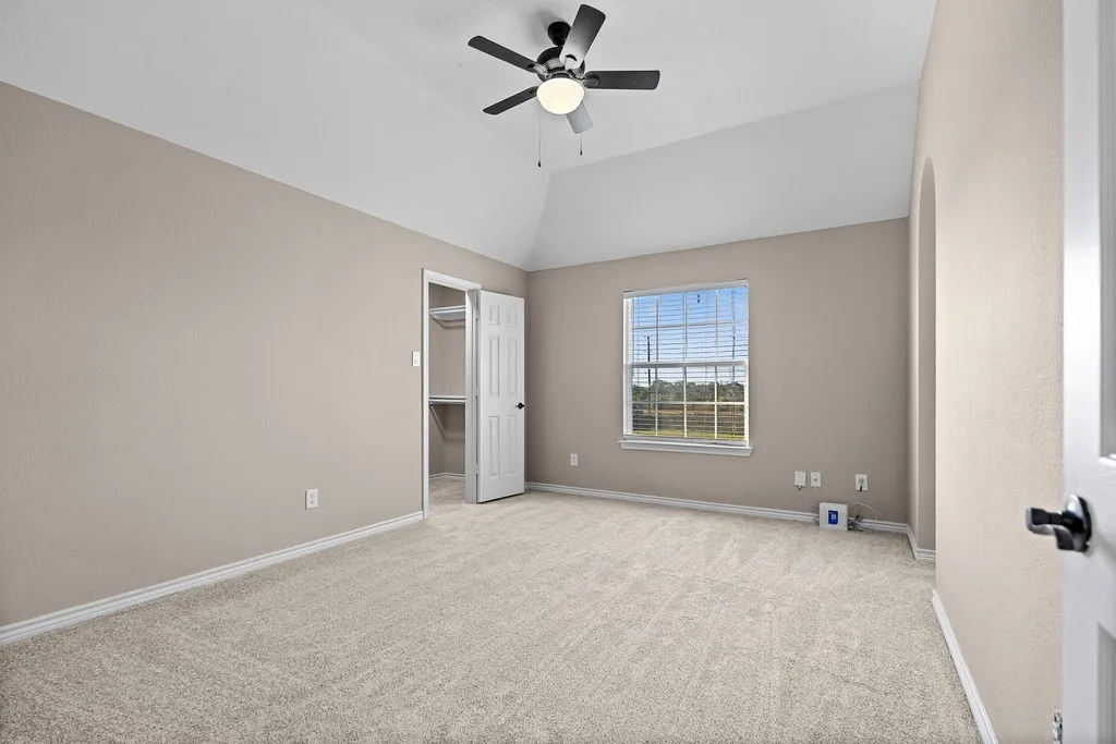 Vaulted ceiling with a ceiling fan, neutral wall color, carpeted flooring, window with blinds, and an arched entryway