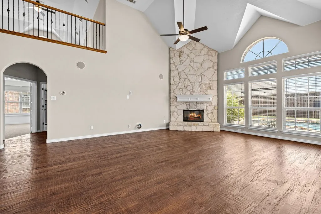 Vaulted ceiling, stone-clad fireplace, wood-finish flooring, and large windows with arched transom