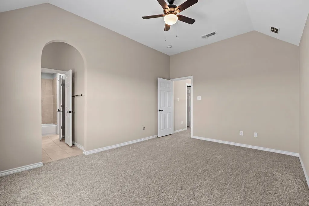 Vaulted ceiling with a ceiling fan, carpet flooring, arched doorway, and white trim