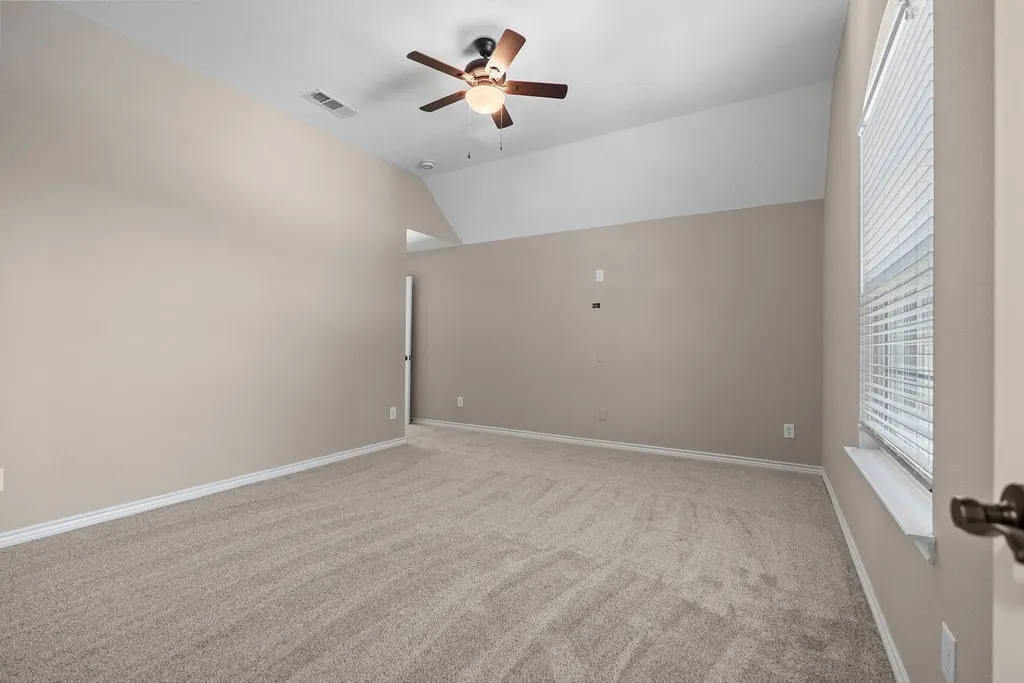 Vaulted ceiling room featuring carpet flooring, neutral-toned walls, and a ceiling fan with integrated lighting