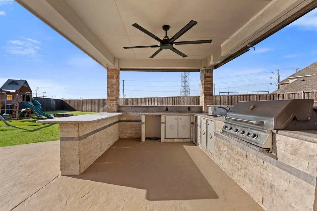 Covered outdoor kitchen featuring a built-in grill, stone-clad island with counter space, integrated storage, and a ceiling fan