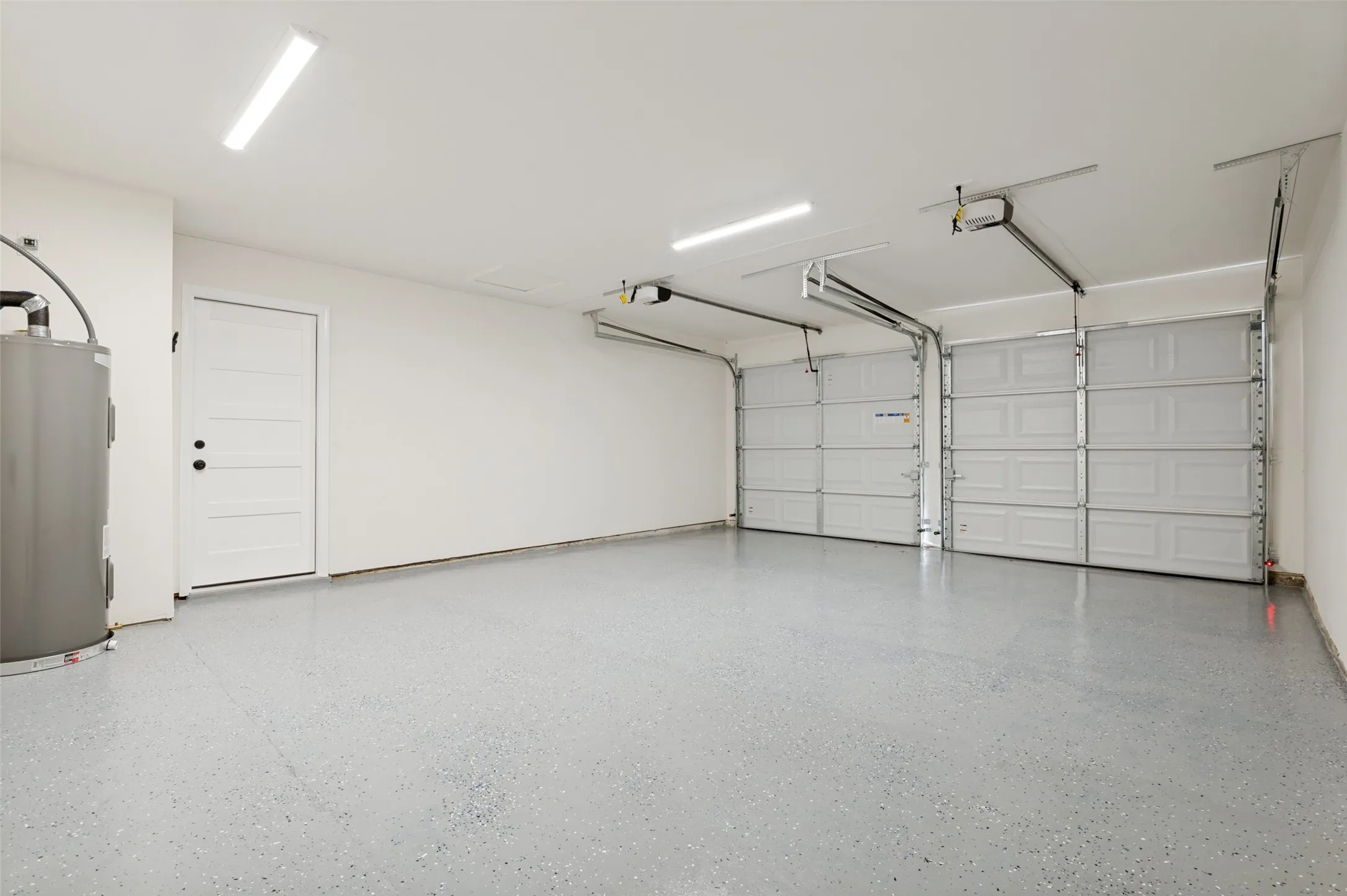 The two-car garage features a gray speckled epoxy floor and is showing off the new water heater.