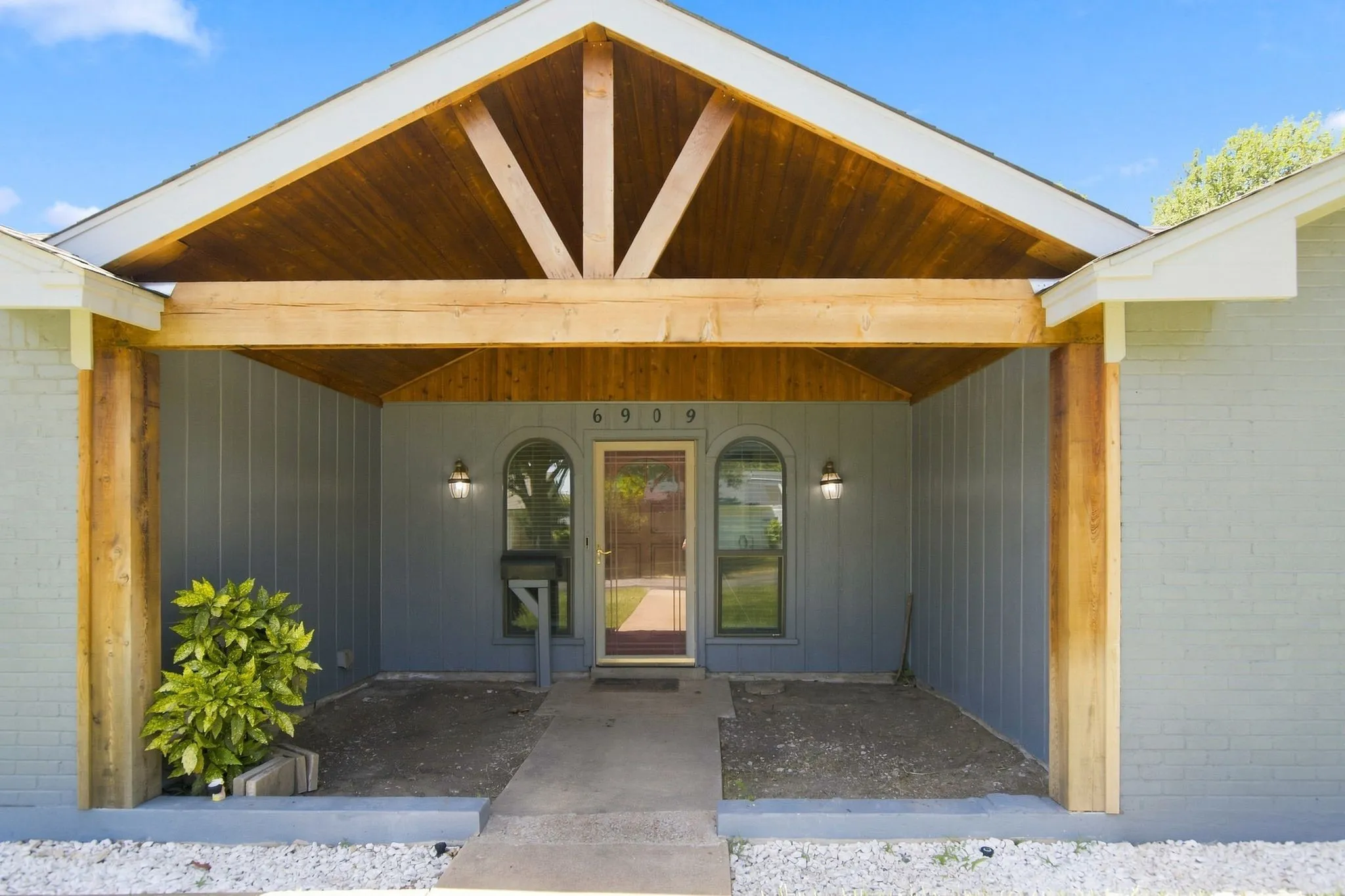 Gable roofline with exposed cedar wood beams, brick facade, covered entry, and twin arched windows