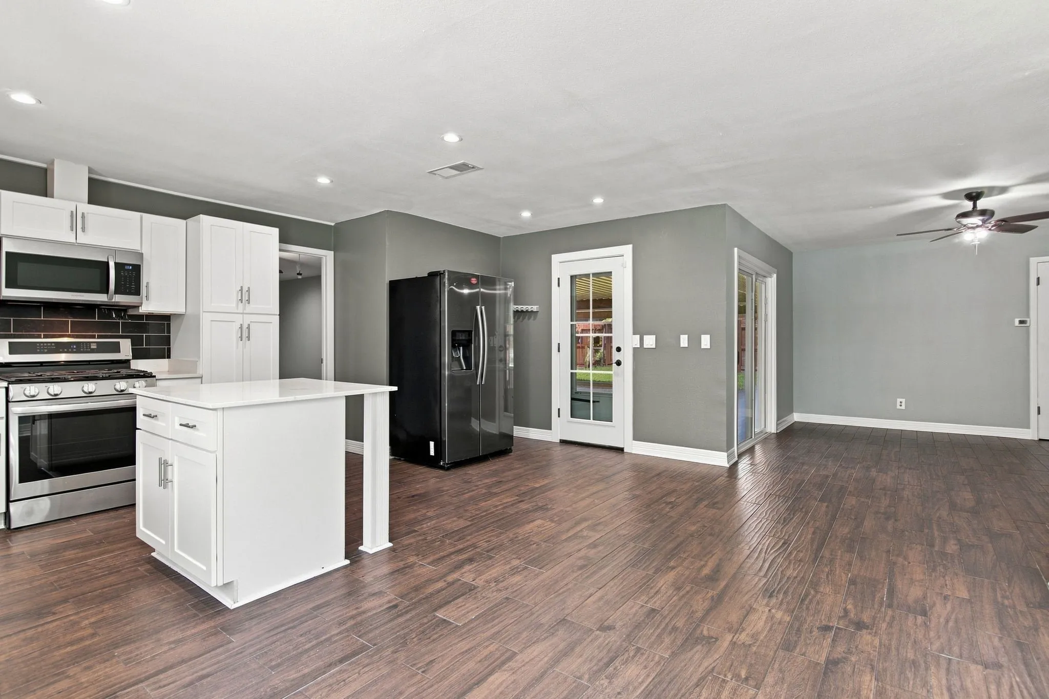 Open-concept living space with wood-finish flooring, white cabinetry, stainless steel appliances, a center island, and a ceiling fan
