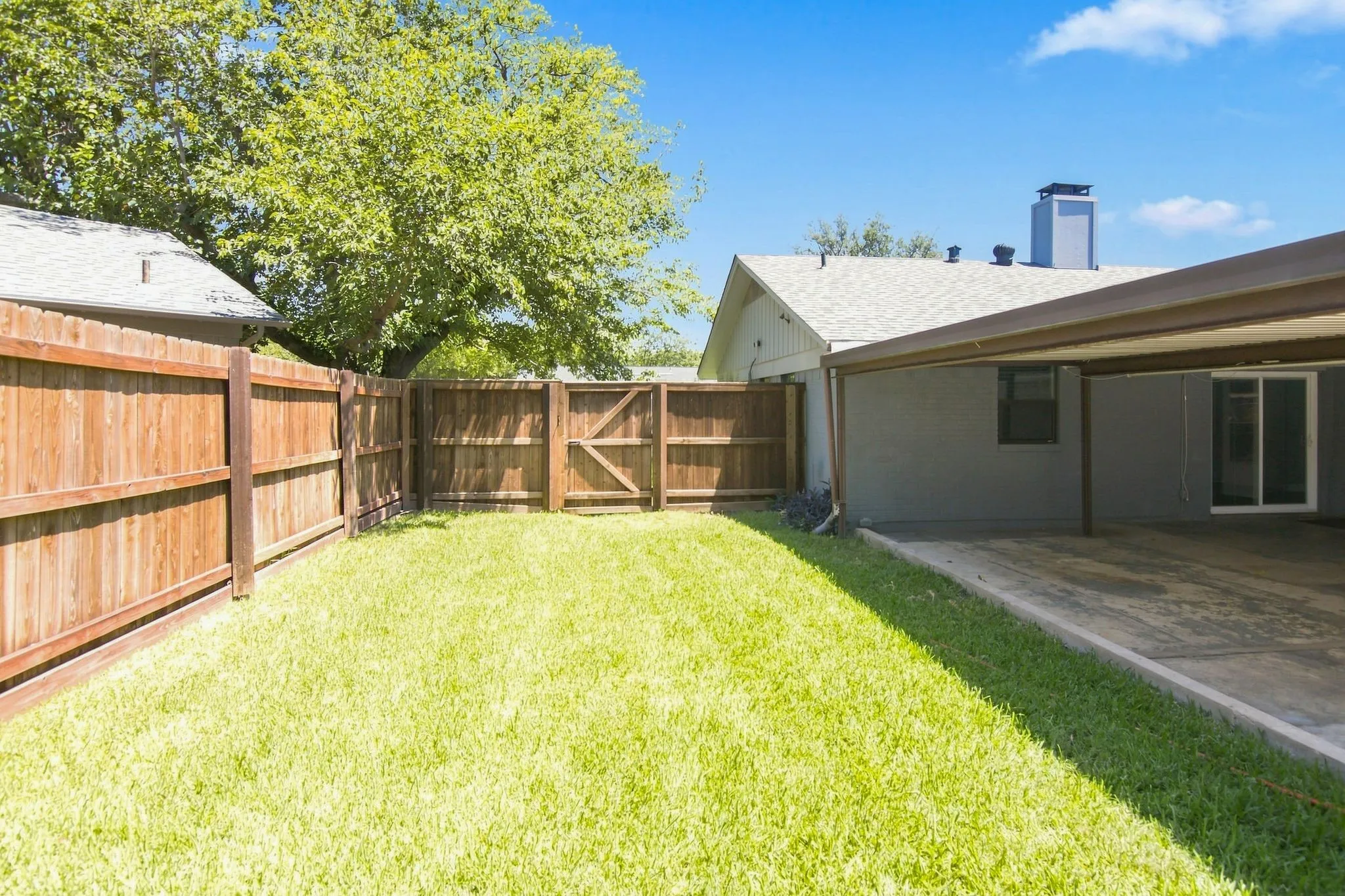 Expansive backyard featuring a manicured lawn, new wood privacy fencing, and a covered carport  area with a concrete surface