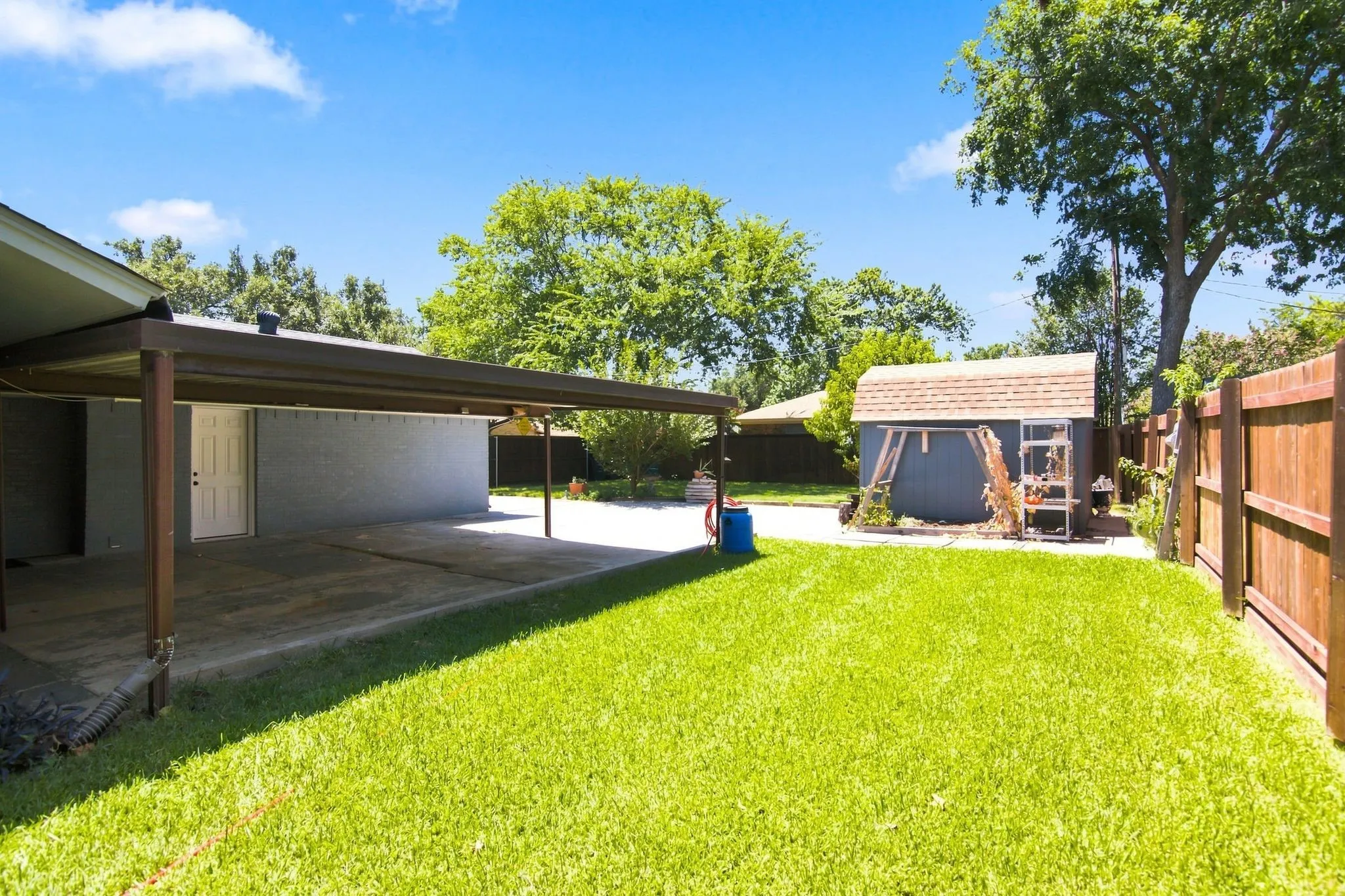 Expansive backyard featuring a lush lawn, concrete patio, and a covered carport