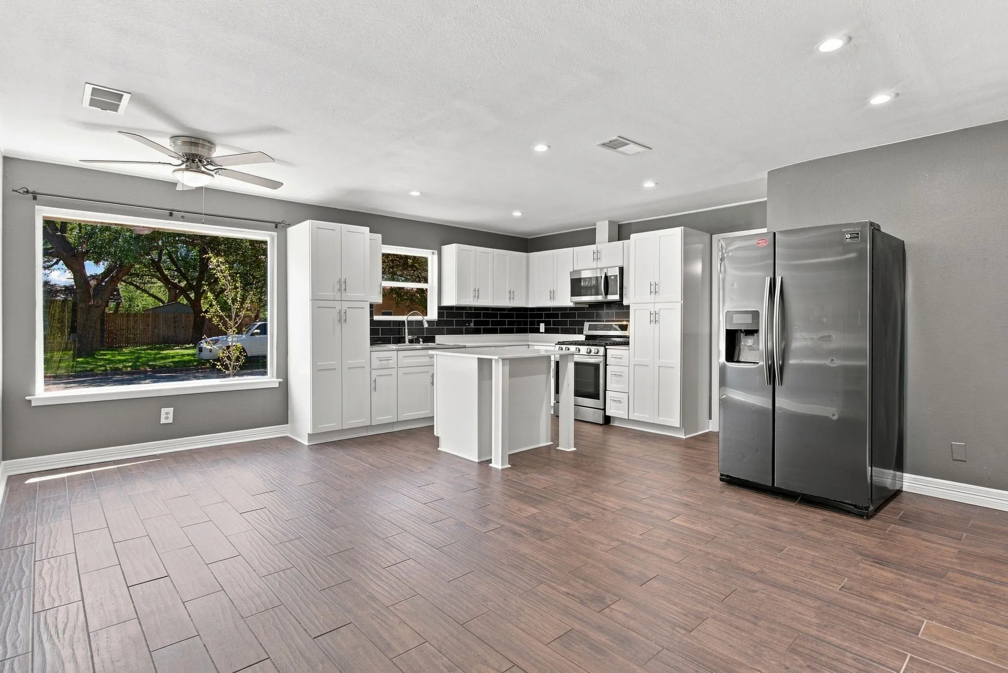 Open-concept living space with wood-finish flooring, white cabinetry, a kitchen island, and stainless steel appliances