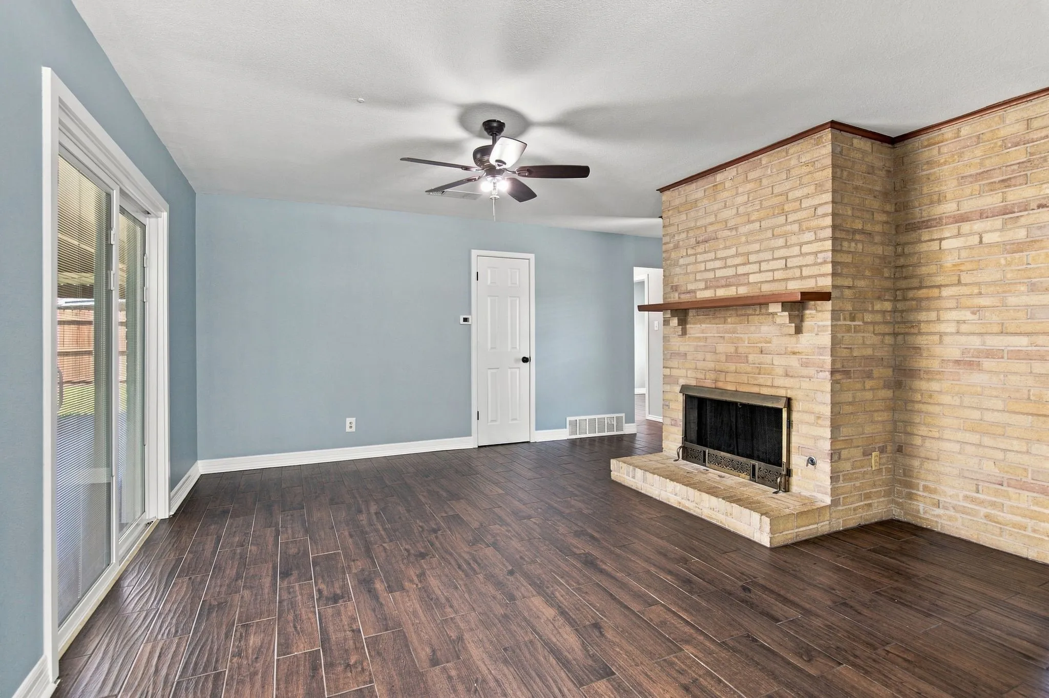 Brick fireplace with a wood-finish mantel and hearth, wood-finish flooring, and white trim