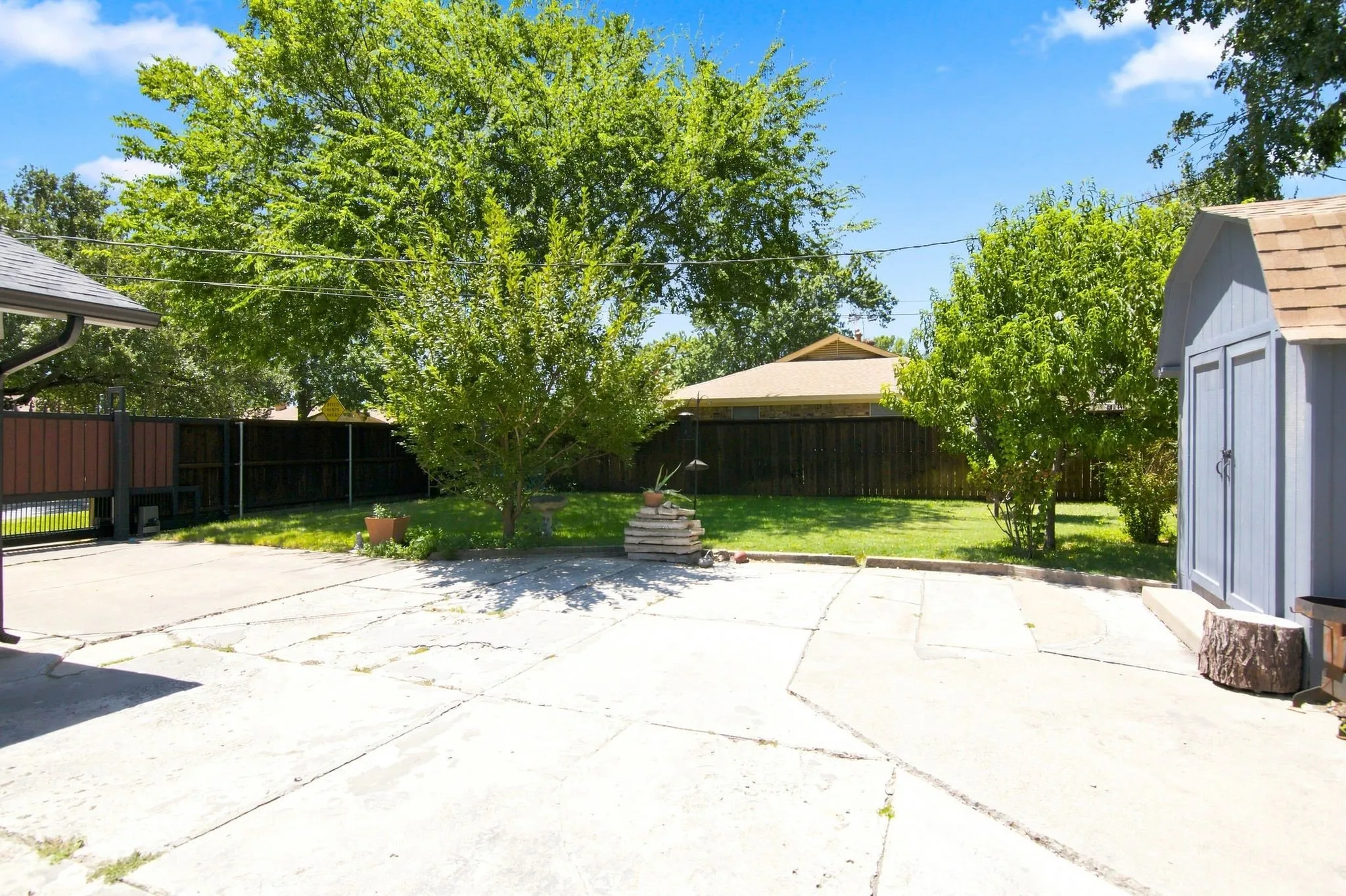 Expansive concrete patio with a spacious grassy area, perimeter fencing, electric gate and mature trees