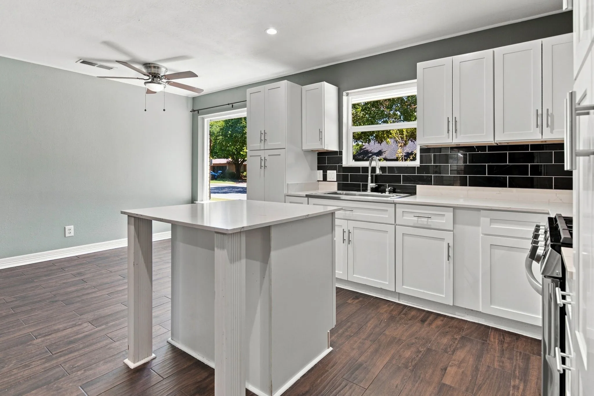 Kitchen featuring white cabinetry,quartz countertops, a black subway tile backsplash, and wood-finish tile flooring