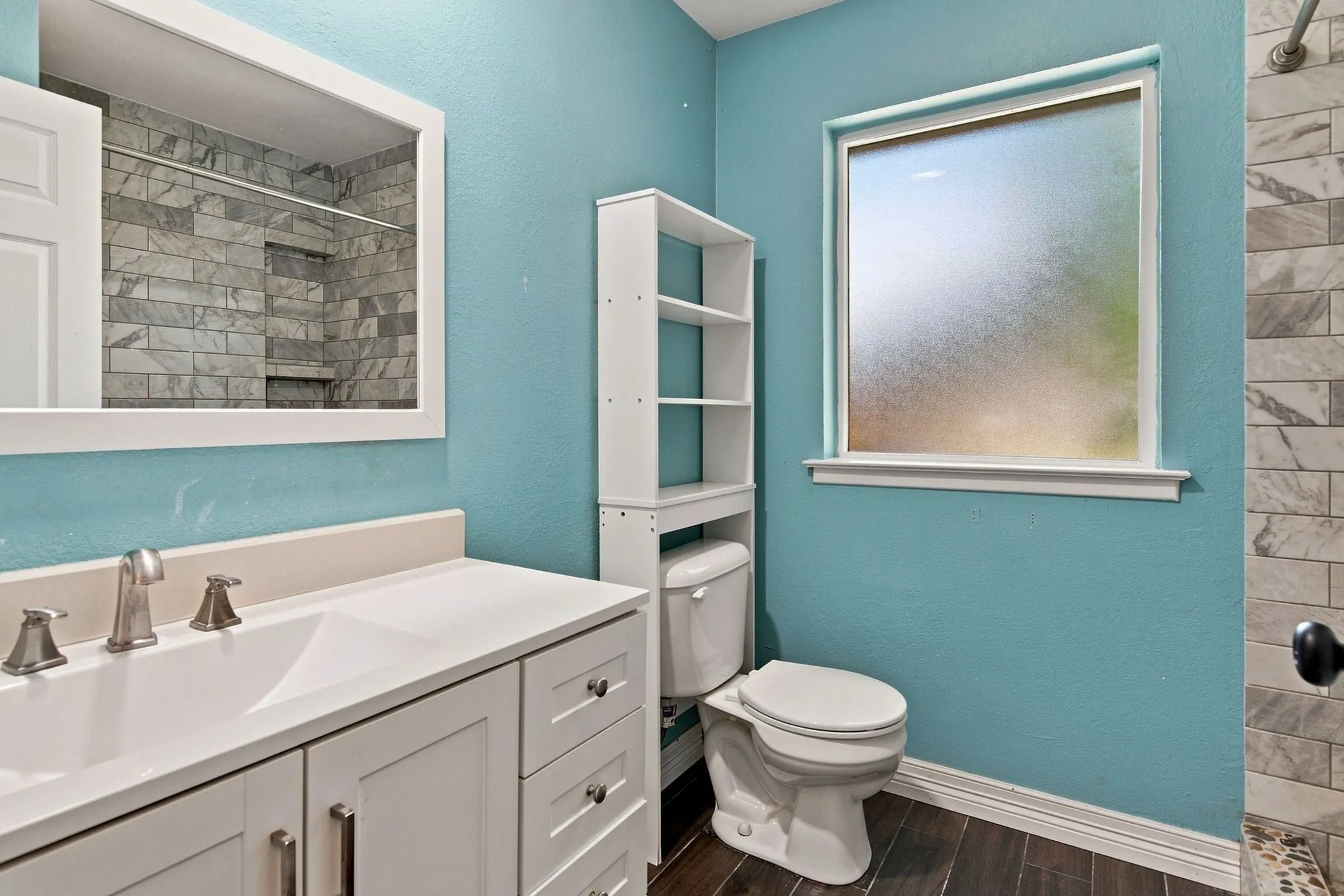 Vanity with an integrated sink and brushed nickel faucet, wood-finish flooring, and a tiled shower with recessed shelving