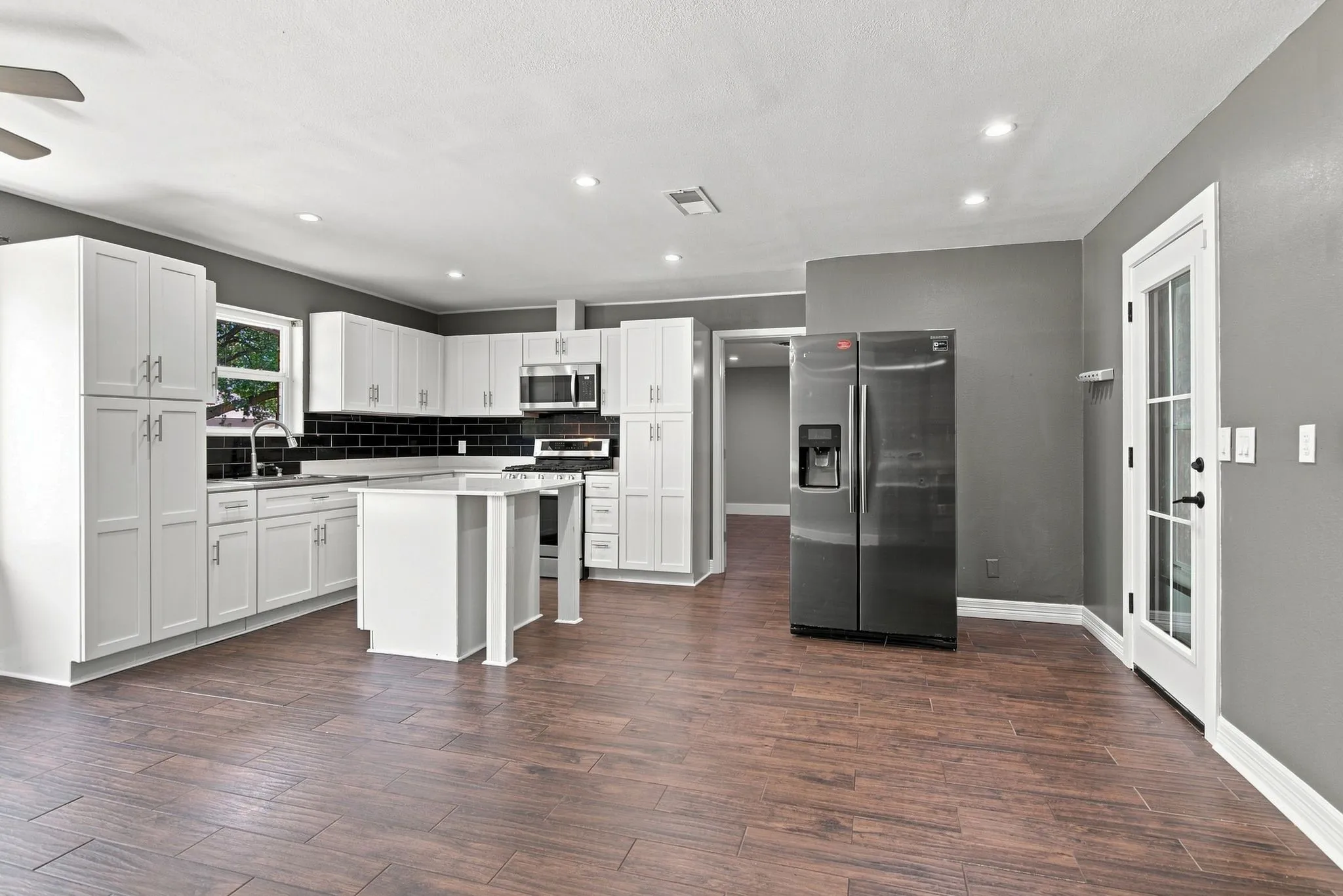 White shaker cabinetry, stainless steel appliances, dark subway tile backsplash, wood-finish tile flooring, and recessed lighting