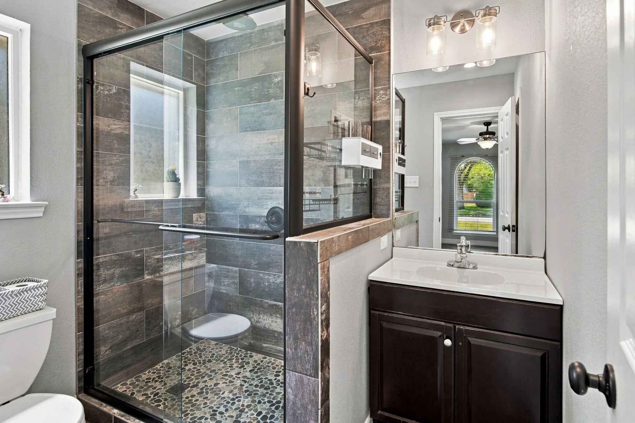 Glass-enclosed shower with pebble-finish flooring and tile surround shower area