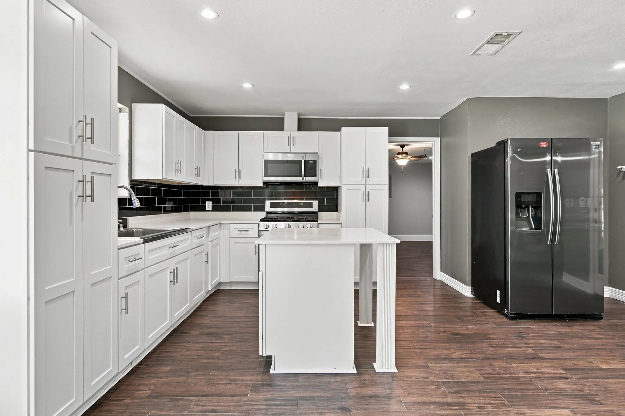 Kitchen featuring white cabinetry, dark subway tile backsplash, white countertops, a central island, and wood-finish flooring