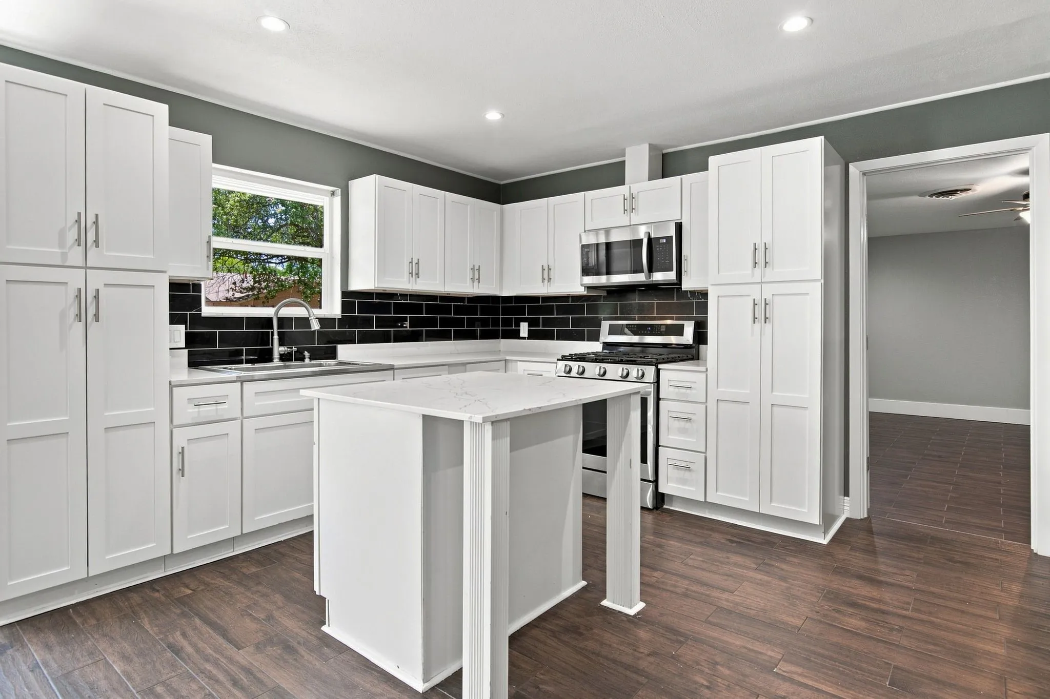 Kitchen featuring white cabinetry, a central island, stainless steel appliances, a black subway tile backsplash, and wood-finish flooring