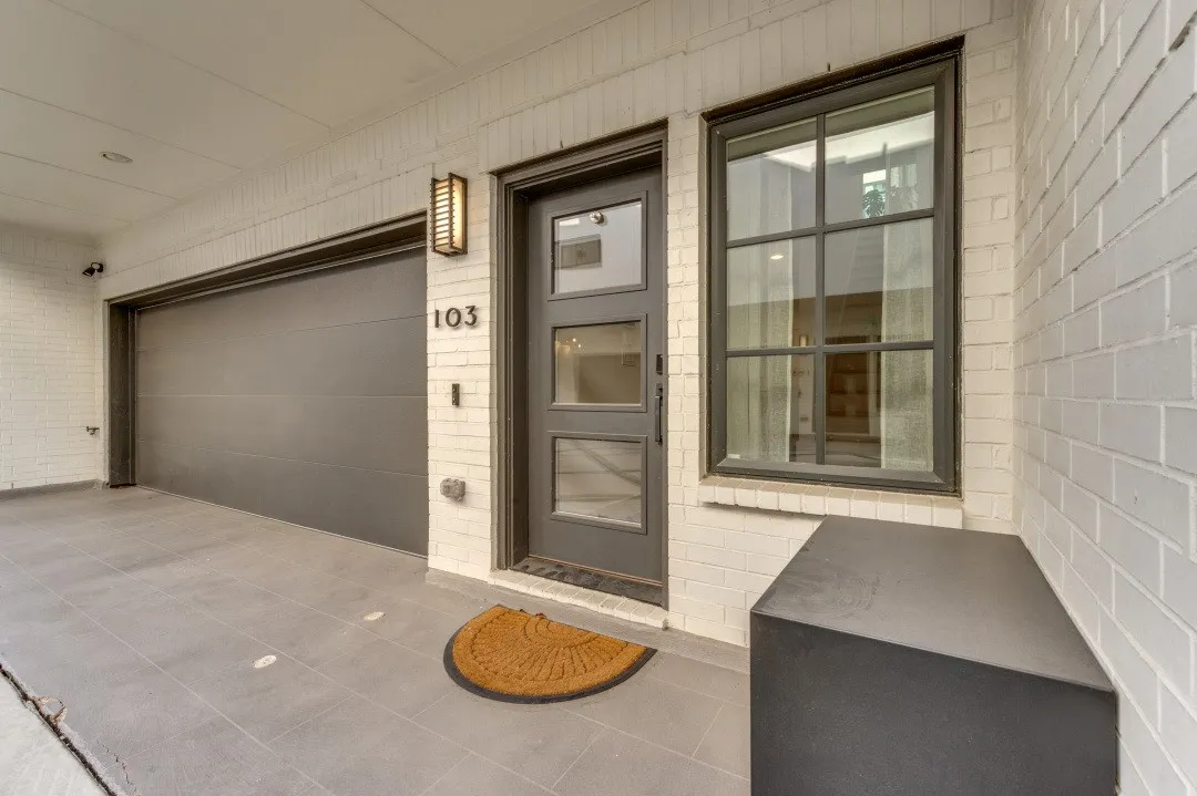 White brick exterior with a dark gray garage door, modern entry door with glass panels, and an exterior wall sconce
