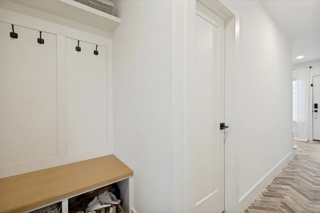 Built-in bench with cubby storage, wall paneling with hooks, and herringbone tile flooring