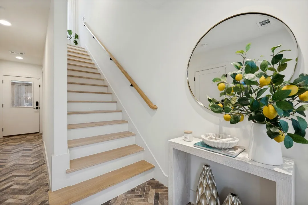 Herringbone wood-finish flooring, staircase with wood treads and white risers, light wood handrail, recessed lighting, and a white entry door with frosted glass insert