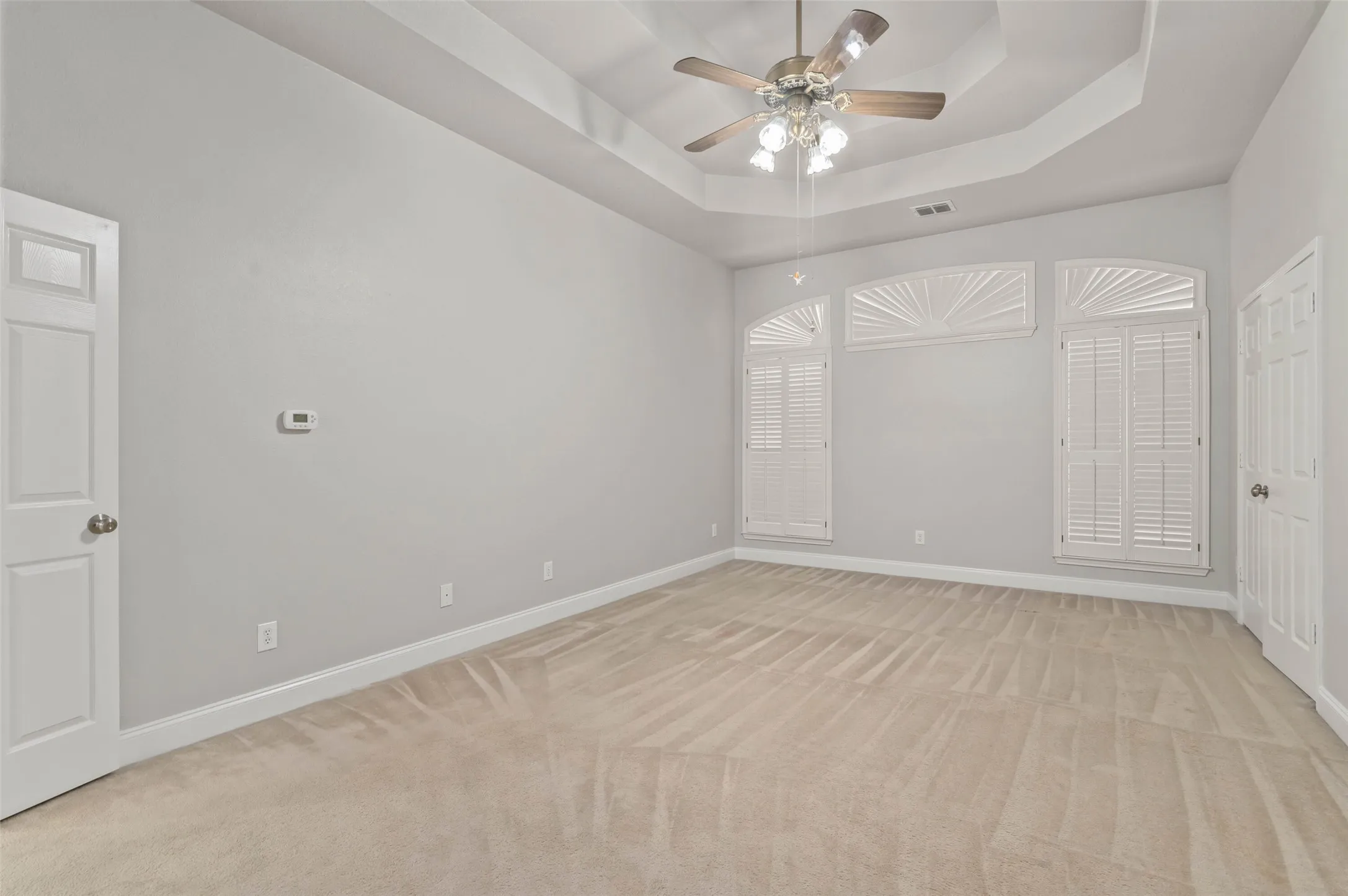 Huge primary bedroom with carpeted flooring, ceiling fan and large picture windows.