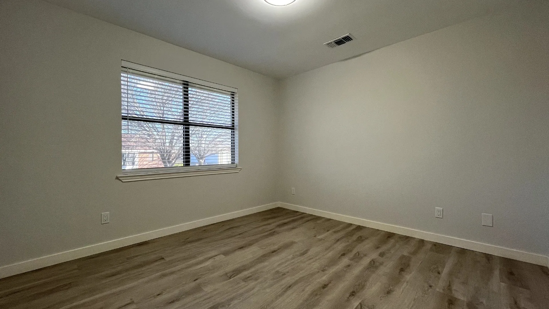 Recessed window with blinds, wood-finish flooring, and a flush-mount ceiling light