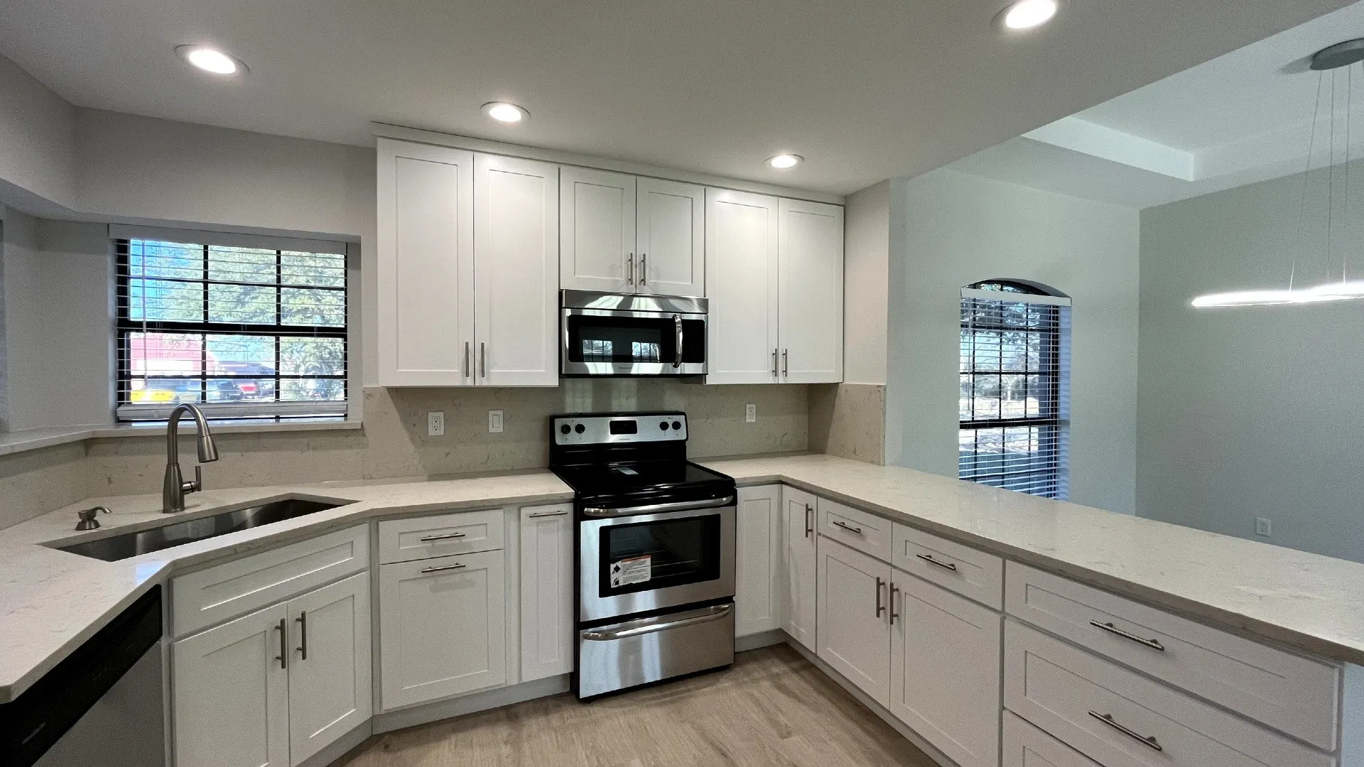 White shaker cabinetry, light-toned countertops, stainless steel appliances, recessed lighting, and wood-finish flooring