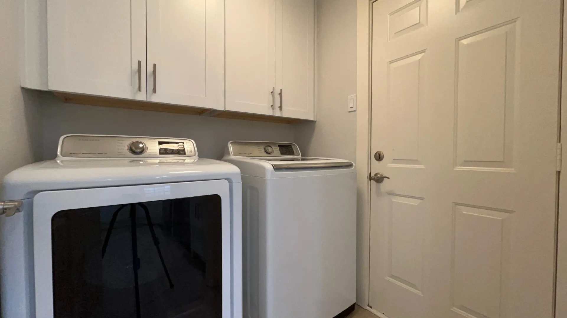 White shaker-style cabinetry with brushed nickel hardware, light wood-finish shelving, and a two-panel door