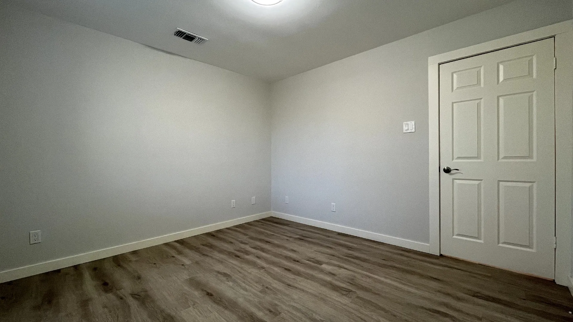 Wood-finish flooring, white trim, recessed ceiling lighting, and a six-panel interior door