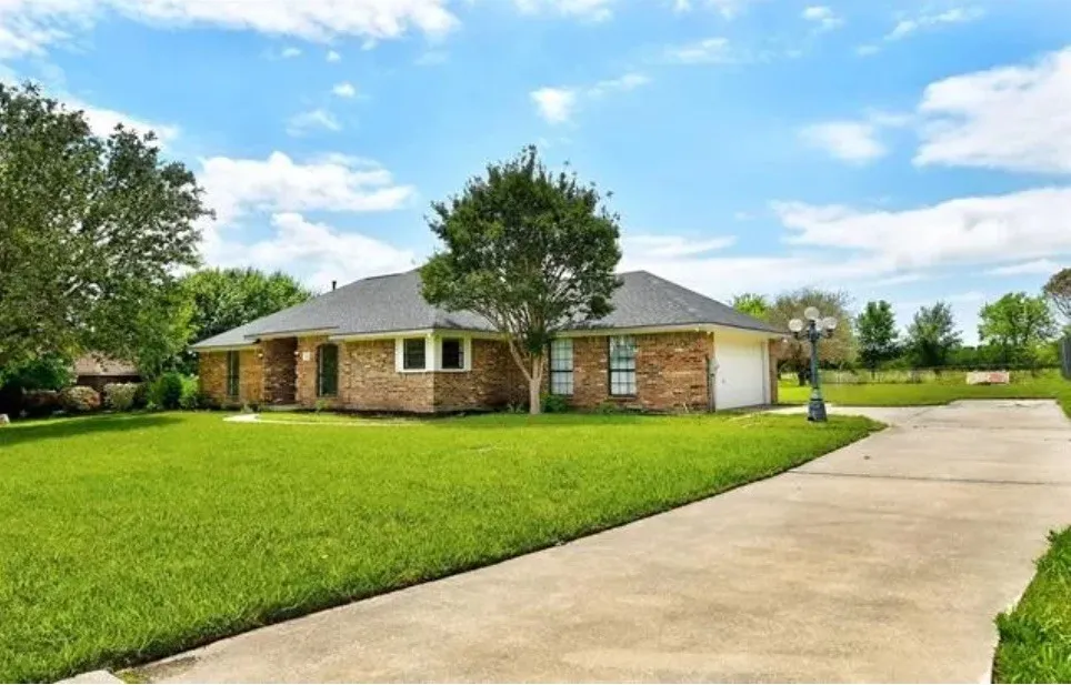 Brick exterior with a dark shingle roof, expansive front lawn, mature trees, and a concrete driveway