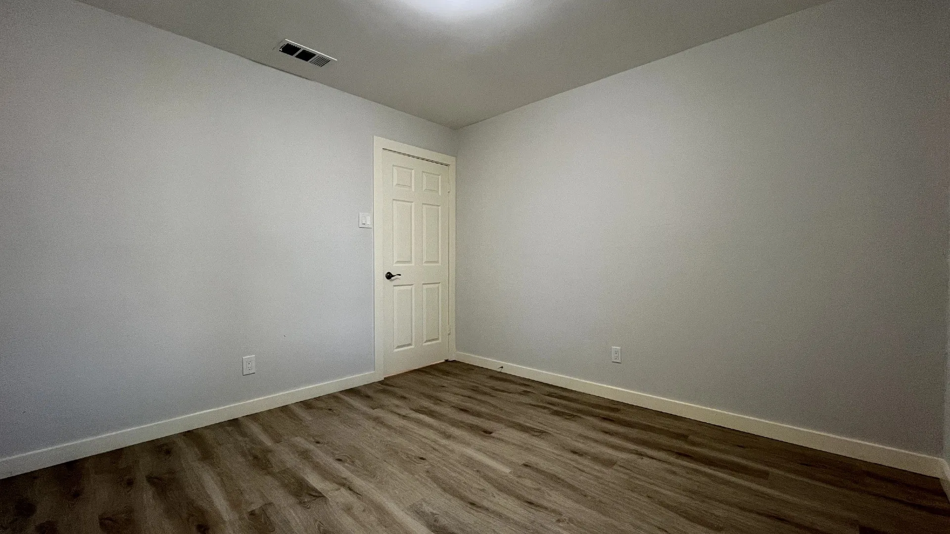 Neutral wall color, wood-finish flooring, and a paneled interior door with dark hardware