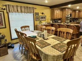 Open-concept dining area featuring a large window with blinds, tile flooring, and integrated wood cabinetry